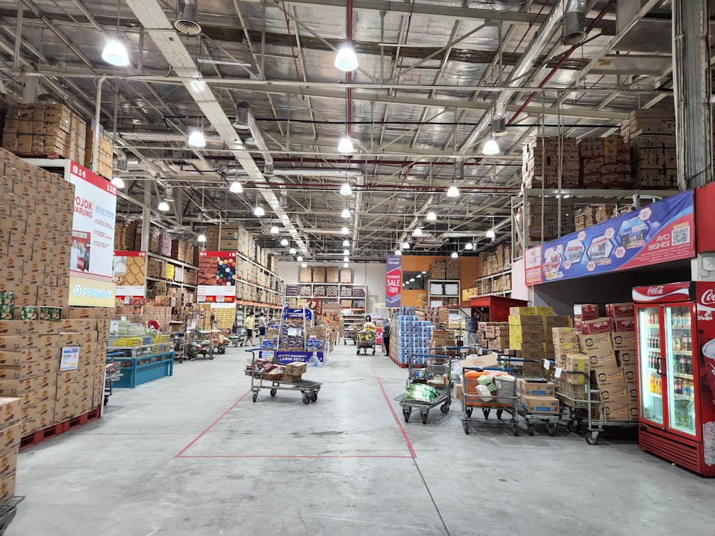 Explore a bustling warehouse filled with stacked goods and shopping carts, illuminated under bright lighting.
